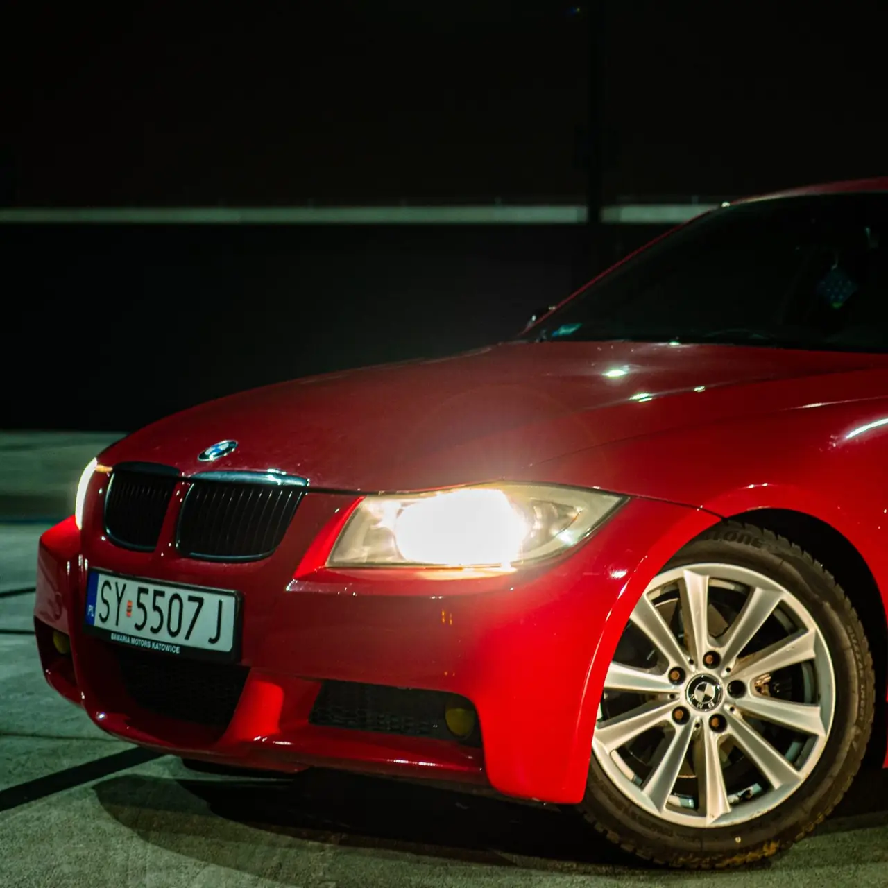 Czerwone BMW nocą z zapalonymi reflektorami